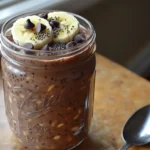 Jar of chocolate protein overnight oats topped with banana and chocolate chips